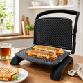 Gril panini Taurus Rockstone ouvert avec deux paninis dorés sur table en bois avec thé et assiette