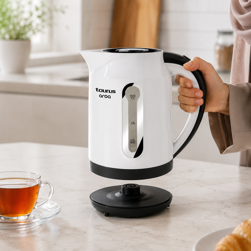 Main saisissant la bouilloire Taurus Aroa sur son socle rotatif 360° avec tasse de thé